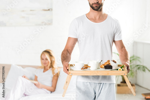 panoramic shot of man holding food tray with breakfast in bedroom