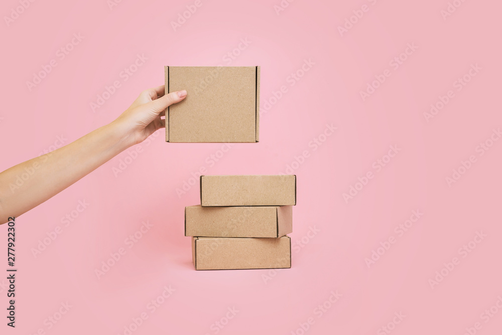 Woman&rsquo;s hands holding boxes stacked on pale pink background. Mock up