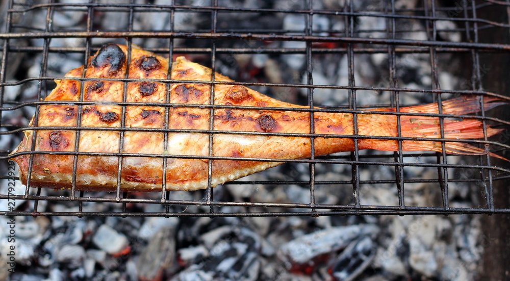 Spicy marinated sea bass grilling over the hot coals on a barbecue for a summer picnic. Fried fish on fire close-up. Selective focus, top view.