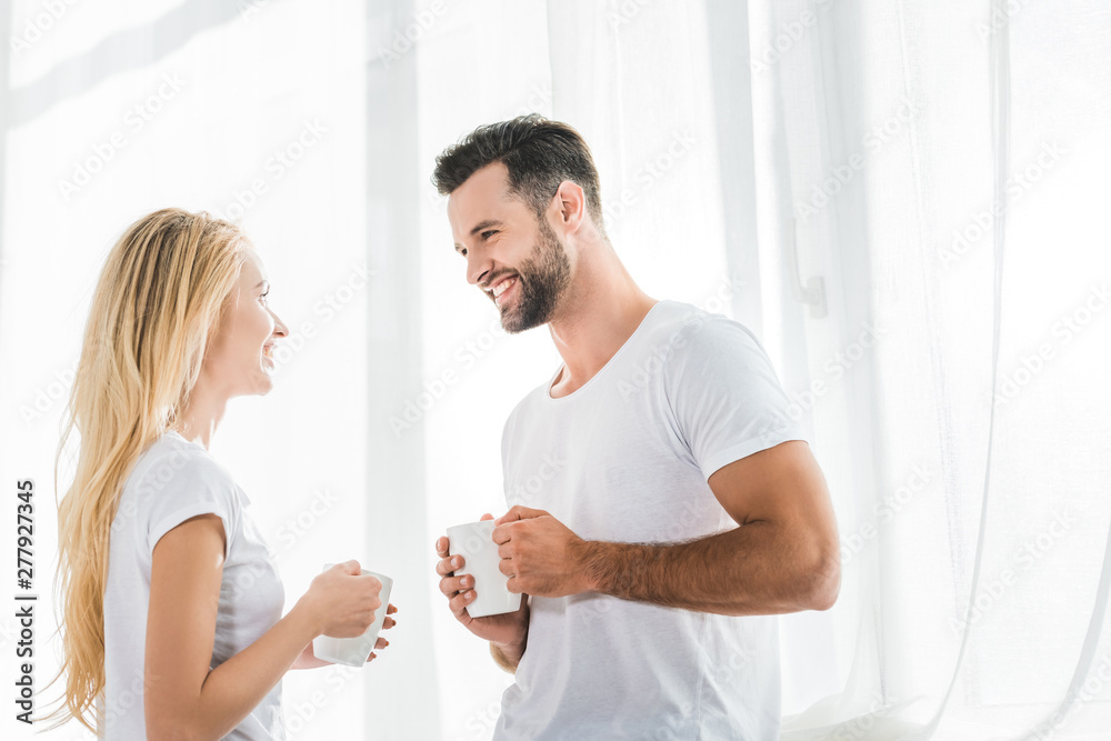 beautiful couple with coffee cups looking at each other at home in morning beautiful couple with coffee cups looking at each other at home in morning