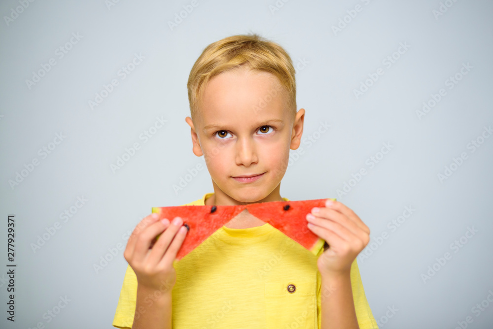 Smart caucasian 5 year old boy in yellow t-shirt holding two pieces of red watermelon as a bow tie, horizontally. Smart caucasian 5 year old boy in yellow t-shirt holding two pieces of red watermelon as a bow tie, horizontally.