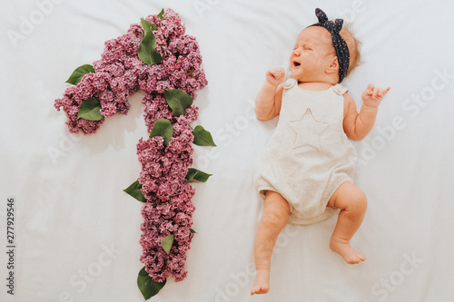 Flat lay picture of a 1 month baby with number made out of oak leaves and lilac flower