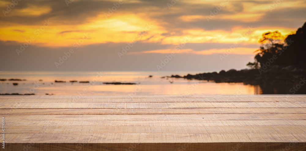 Empty wooden bar counter with blurred sunset beach background.