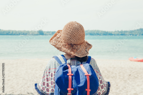 Back side view of the happy young woman in straw hat siting and relaxing on the beach. photo