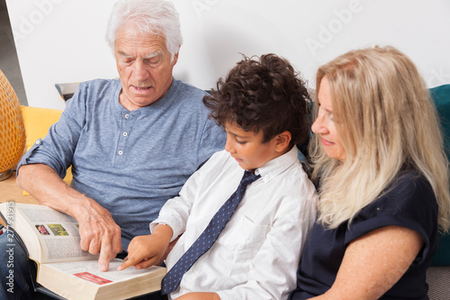 GRANDS PARENTS AVEC LEUR PETIT FILS REGARDANT UN DICTIONNAIRE