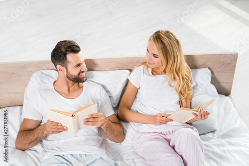 beautiful smiling couple lying in bed with books at home