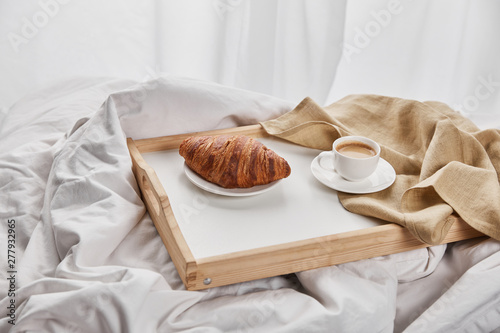 fresh croissant with coffee and napkin on wooden tray in bed at morning #277932965