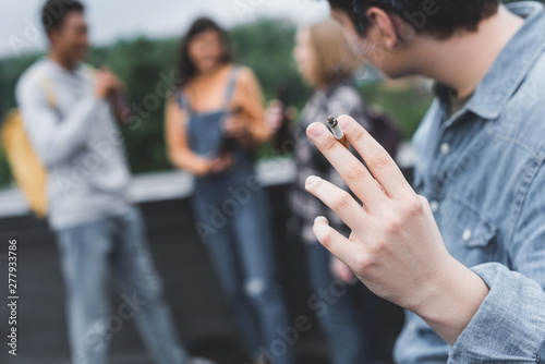 selective focus of teenager smoking cigarette with friends on roof