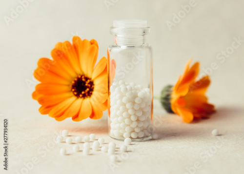 Calendula officinalis, the pot marigold, ruddles, common marigold or Scotch marigold with white round homeopathy pills in medical bottle. 