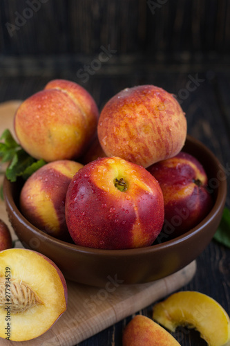 Delicious juicy orange-red peaches and nectarines on a dark background in a clay bowl. Dark background  still life of ripe summer fruits on a brown wooden table. Vertical photo