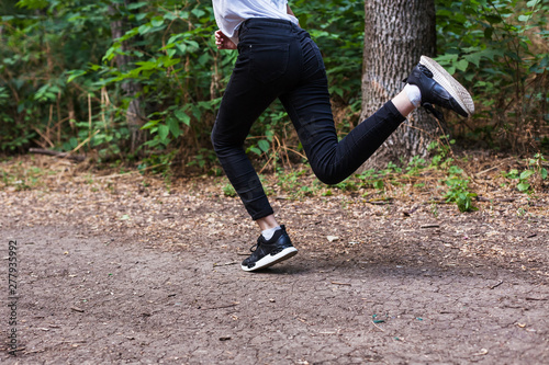 young girl in a white t-shirt in black jeans and sneakers running on the forest road
