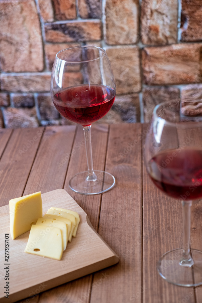 two glasses of red wine and sliced cheese on a wooden table