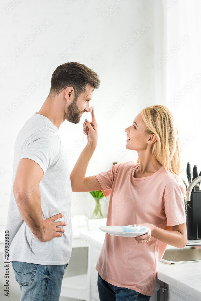 beautiful woman putting foam on smiling man at kitchen in morning beautiful woman putting foam on smiling man at kitchen in morning
