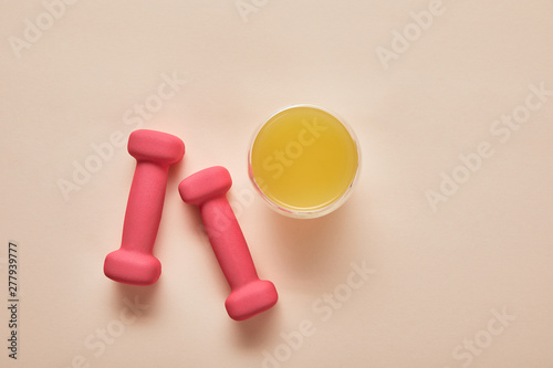 top view of pink dumbbells, orange juice on beige background