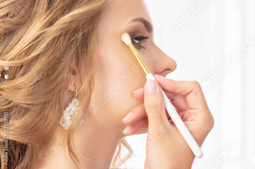 Makeup artist puts makeup on girl model. Brush applies shadows  concealer. beautiful girl model  portrait. Nude colors in makeup. wedding makeup  evening makeup.
