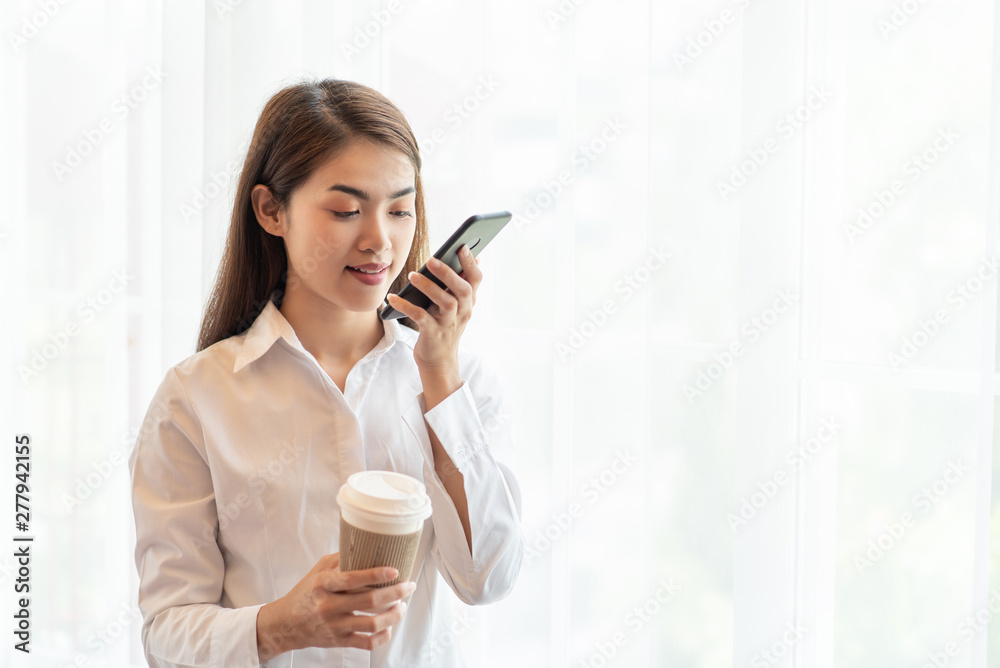 Young Asian woman using mobile phone and holding a hot cup of coffee Young Asian woman using mobile phone and holding a hot cup of coffee