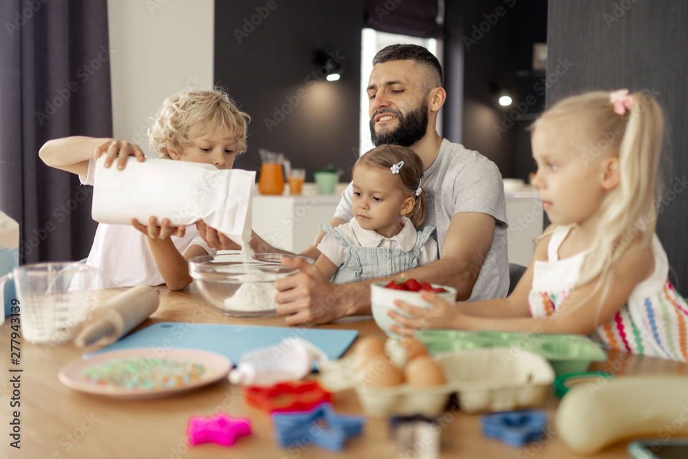 Nice young boy putting flour in the bowl Nice young boy putting flour in the bowl