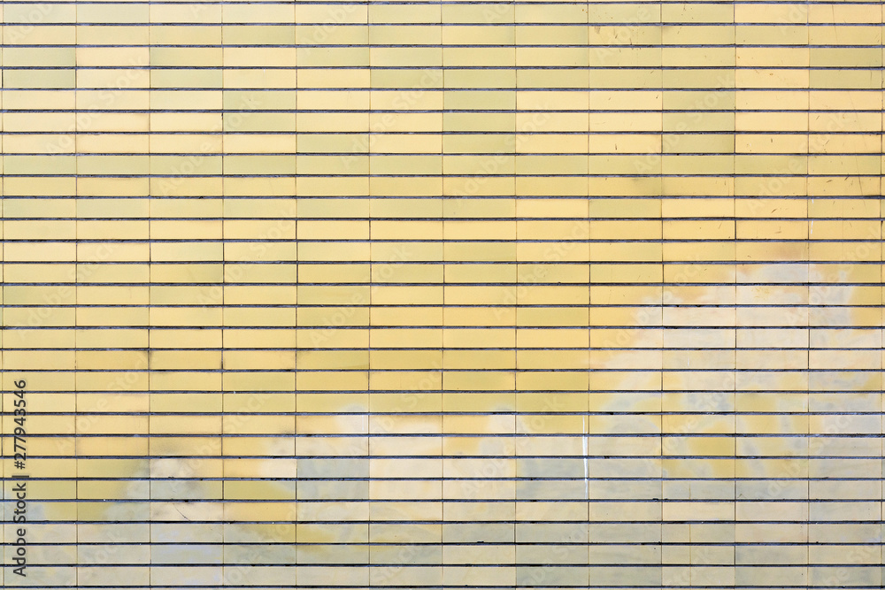 Old yellow tiled brick surface with washed out graffiti on the lower part Old yellow tiled brick surface with washed out graffiti on the lower part