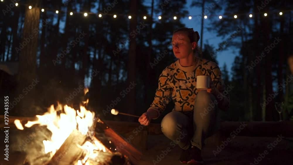 Woman with cup fries marshmallows on the fire near the tent. Woman with cup fries marshmallows on the fire near the tent.
