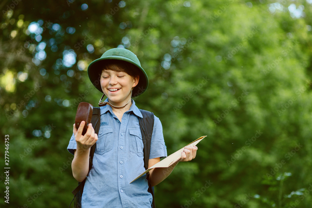 Portrait of little explorer with map and compass in forest. Boy traveler in helmet play in the park. Happy child go hiking with backpack in summer nature. Dream concept. Portrait of little explorer with map and compass in forest. Boy traveler in helmet play in the park. Happy child go hiking with backpack in summer nature. Dream concept.
