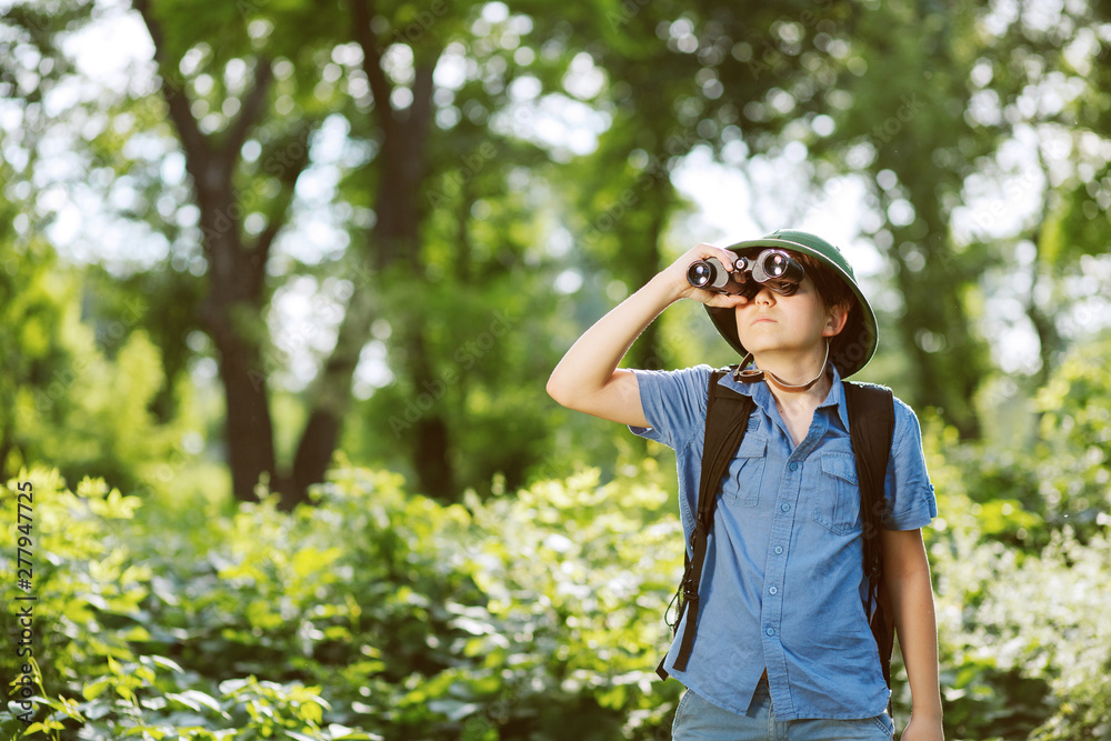 Portrait of little explorer with binoculars in forest. Boy traveler in helmet play in the park. Happy child go hiking with backpack in summer nature. Dream concept. Portrait of little explorer with binoculars in forest. Boy traveler in helmet play in the park. Happy child go hiking with backpack in summer nature. Dream concept.