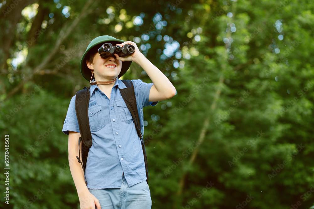 Portrait of little explorer with binoculars in forest. Boy traveler in helmet play in the park. Happy child go hiking with backpack in summer nature. Dream concept. Portrait of little explorer with binoculars in forest. Boy traveler in helmet play in the park. Happy child go hiking with backpack in summer nature. Dream concept.