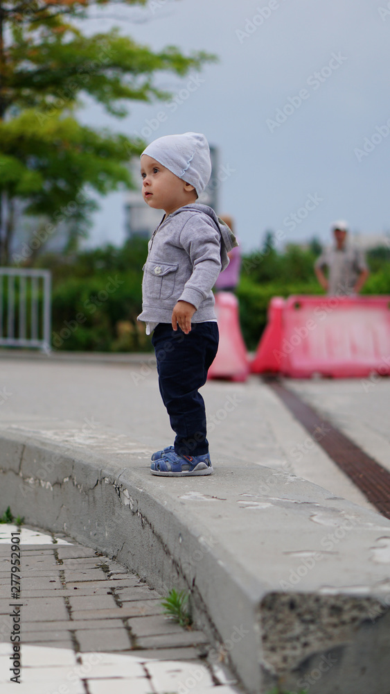 Baby boy in white hat standing on parapet in square