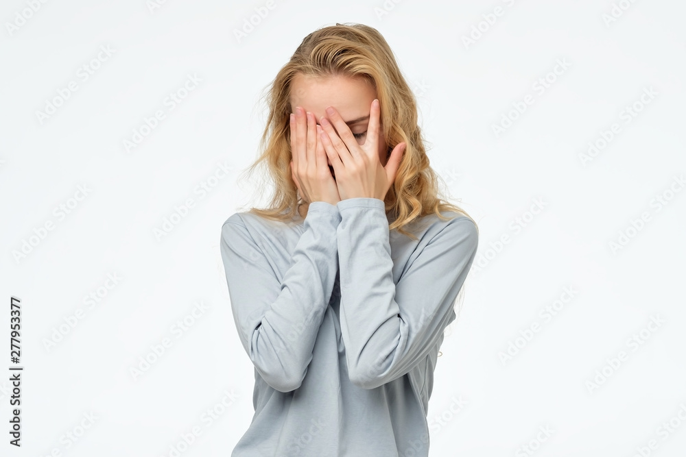 Scared caucasian teen girl in blue pulover hiding her face in hands, isolated on white background. Negative facial human emotion. Scared caucasian teen girl in blue pulover hiding her face in hands, isolated on white background. Negative facial human emotion.