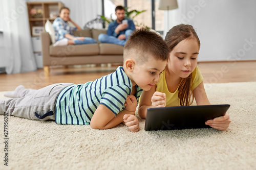 childhood, technology and family concept - brother and sister with tablet computer lying on floor at home