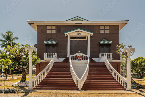 Puerto Princesa, Palawan, Philippines - March 3, 2019: Iwahig Penal Colony. Closeup of brown and white iconic Recreation Hall with broad staircase under blue sky. Green foliage. photo