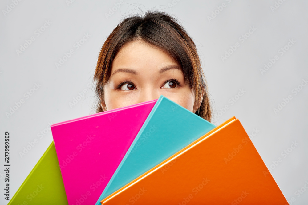 education, school and knowledge concept - asian woman or student girl hiding behind notebooks over grey background education, school and knowledge concept - asian woman or student girl hiding behind notebooks over grey background