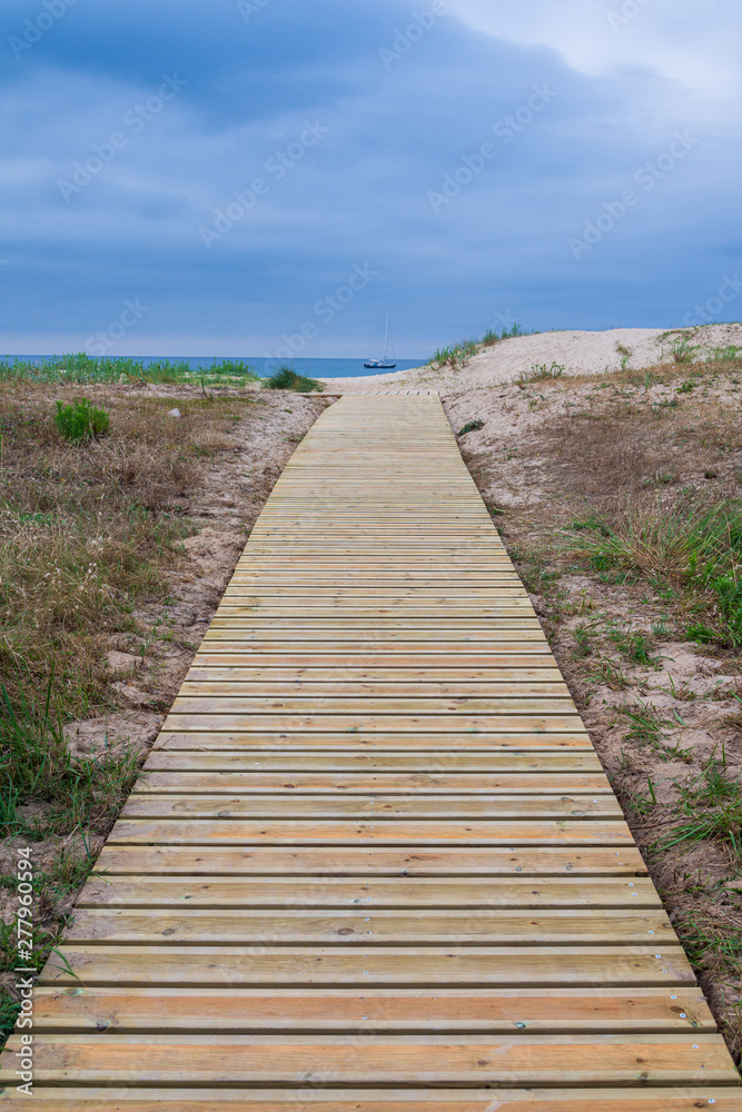 Vertical view of wooden path towards the beach with sea and cloudy sky in the background in Cantabria, Spain, Europe