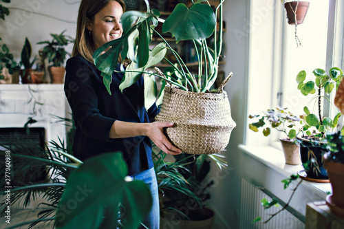 Smiling woman carrying wicker potted plant by window in room at home