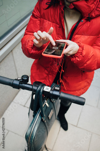 Low section of female commuter scanning QR code on electric push scooter handlebar with smart phone photo