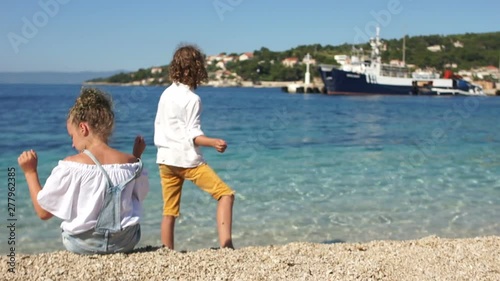 Rear view, schoolchildren curly boy and girl playing with each other on the shores of the Mediterranean. Adriatic, Croatia, Dolmatia region. Travel concept photo