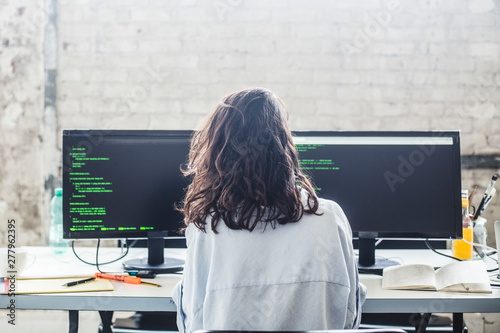 Rear view of female computer hacker coding at desk in creative office photo