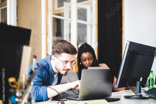 Young computer expert coding in laptop while working with female colleague at workplace