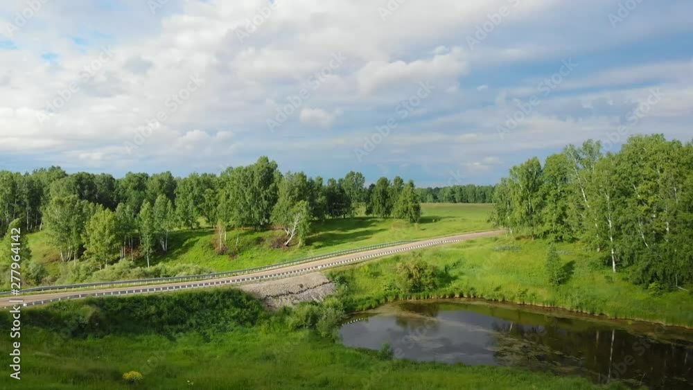 Aerial view. A picturesque view of the reservoir next to small dam and the road through it, surrounded by green vegetation and forest Aerial view. A picturesque view of the reservoir next to small dam and the road through it, surrounded by green vegetation and forest