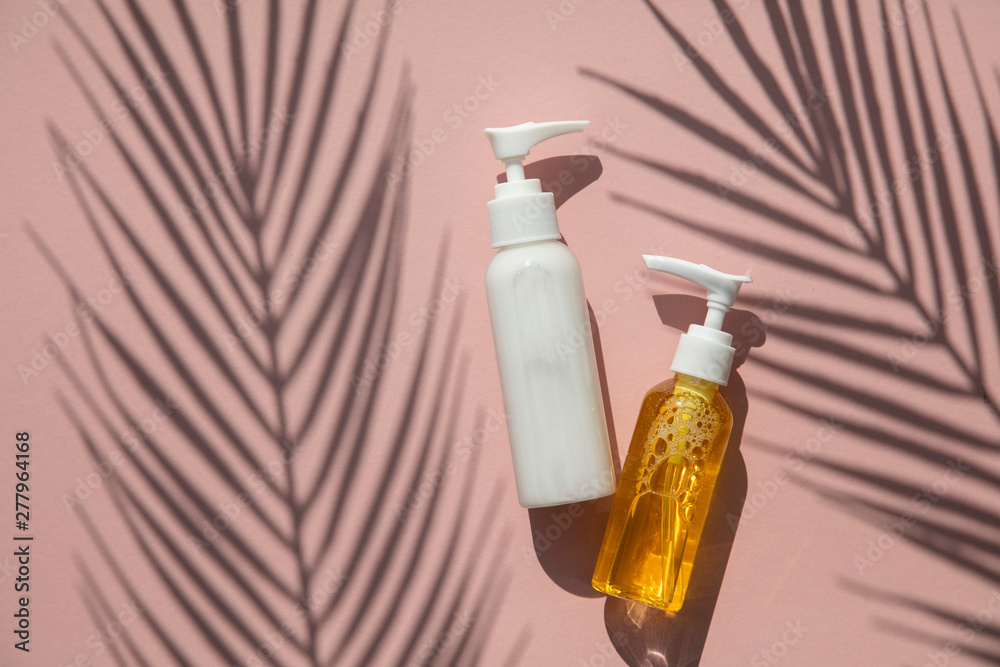 Cosmetic products in bottles on a pink background with tropical palm leaf shadow Cosmetic products in bottles on a pink background with tropical palm leaf shadow