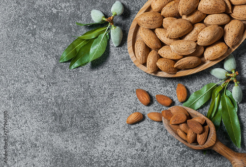Top view Almond nuts in wooden shovel, almonds with shell in bamboo bowl on white table with green fresh raw almonds on almond tree branch Fototapet