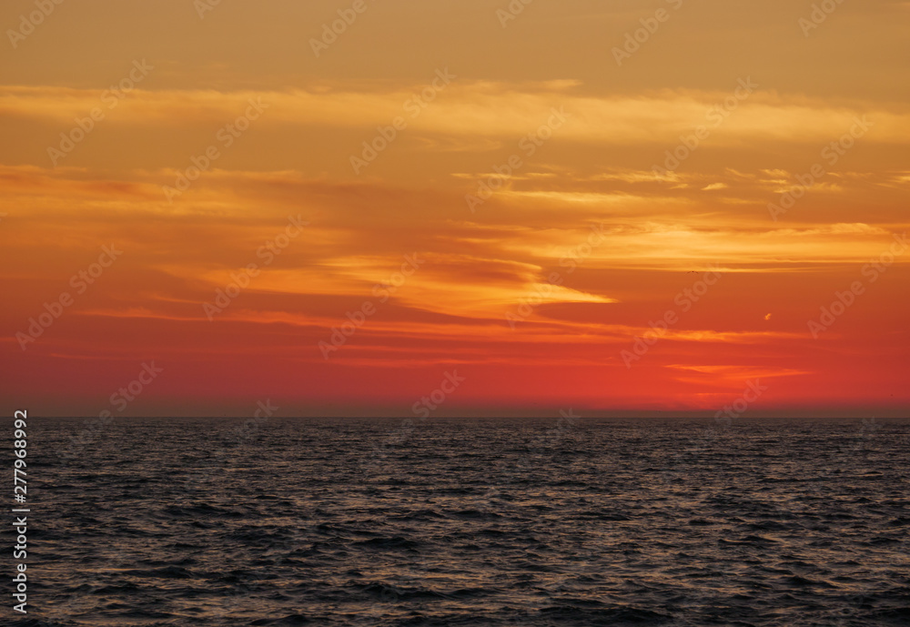 Orange gradient sky at dusk over ocean, just after sunset with dark waves below.