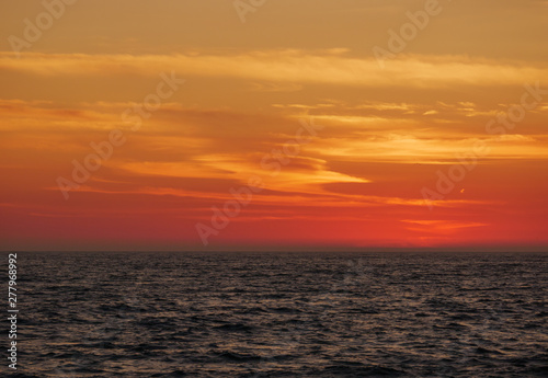 Orange gradient sky at dusk over ocean, just after sunset with dark waves below.