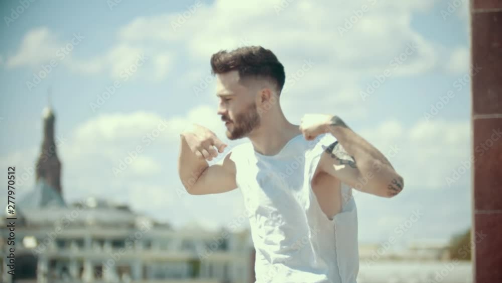 Young stylish man with tattoos in white shirt dancing on the stand on a background of the city Young stylish man with tattoos in white shirt dancing on the stand on a background of the city
