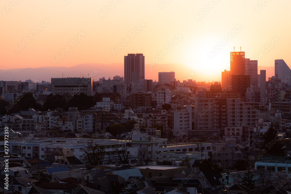 Tokyo, Japan Shinjuku cityscape at sunset with silhouette view of apartment buildings and golden sunlight sun and mountains in background Tokyo, Japan Shinjuku cityscape at sunset with silhouette view of apartment buildings and golden sunlight sun and mountains in background