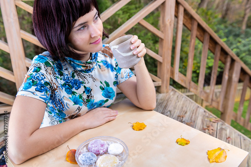 Woman with black asian hair happy smiling sitting at table holding matcha green tea cup outside in backyard garden and daifuku mochi