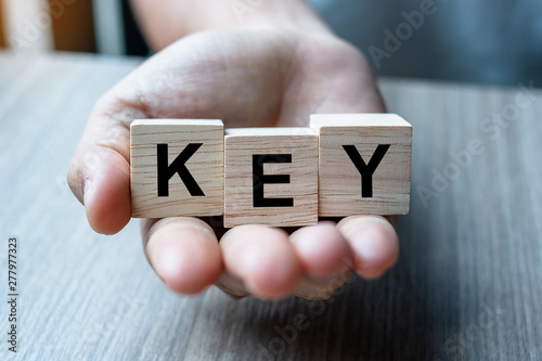 Businessman hand holding wooden cube block with KEY business word on table background. KPI, Performance, indicator and objective concept