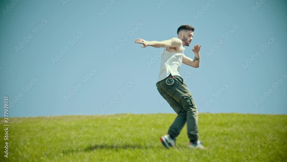 Young stylish man with tattoos in white shirt dancing on the fresh grass Young stylish man with tattoos in white shirt dancing on the fresh grass