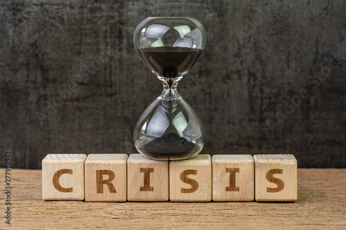 Financial crisis, investment or economic bubble burst countdown concept, sandglass or hourglass on wooden cube block with alphabet building the word Crisis on wood table with dark black background