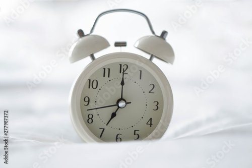 Alarm clock on white bad with light from window, selective focus