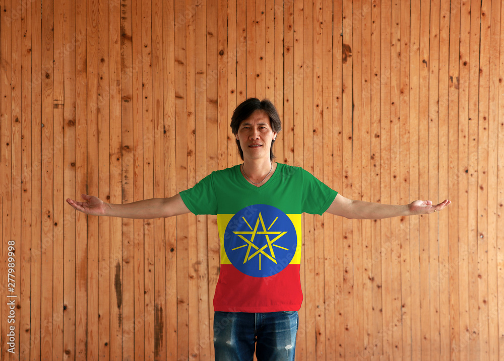 Man wearing Ethiopia flag color shirt and standing with arms wide open on the wooden wall background. Man wearing Ethiopia flag color shirt and standing with arms wide open on the wooden wall background.